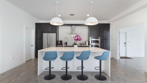 A modern kitchen with a central island, bar stools, and pendant lighting. - Huge Family Retreat w/ Heated Pool & Games (Westlake)