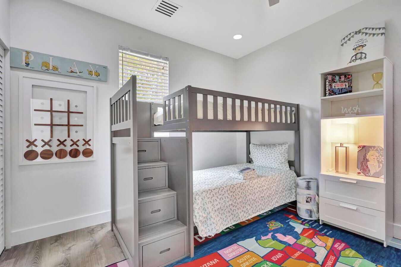 Quarto de criança com cama beliche, cômoda, prateleira com brinquedos e tapete colorido.
