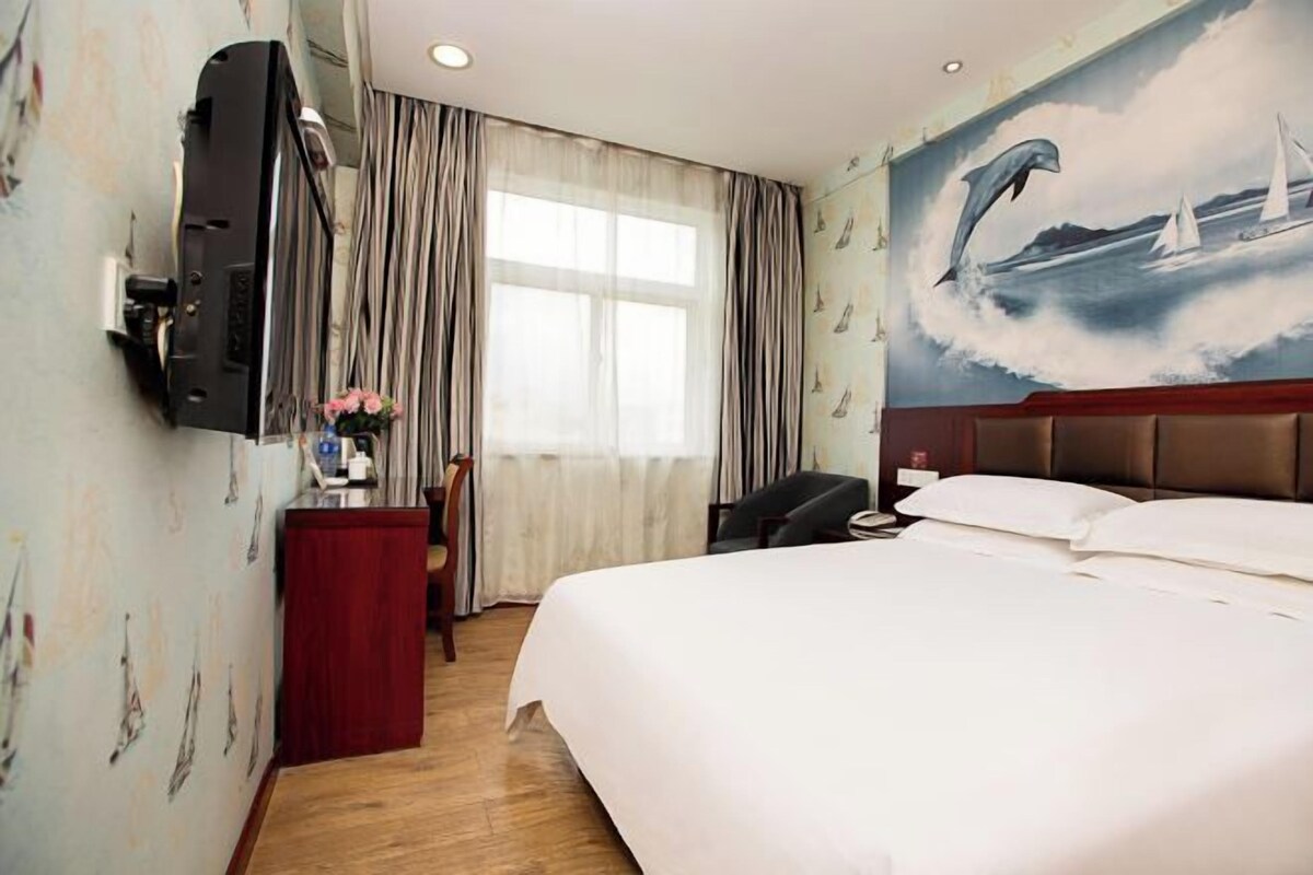 A hotel room with a bed, a desk, a television, and a mural of a dolphin.