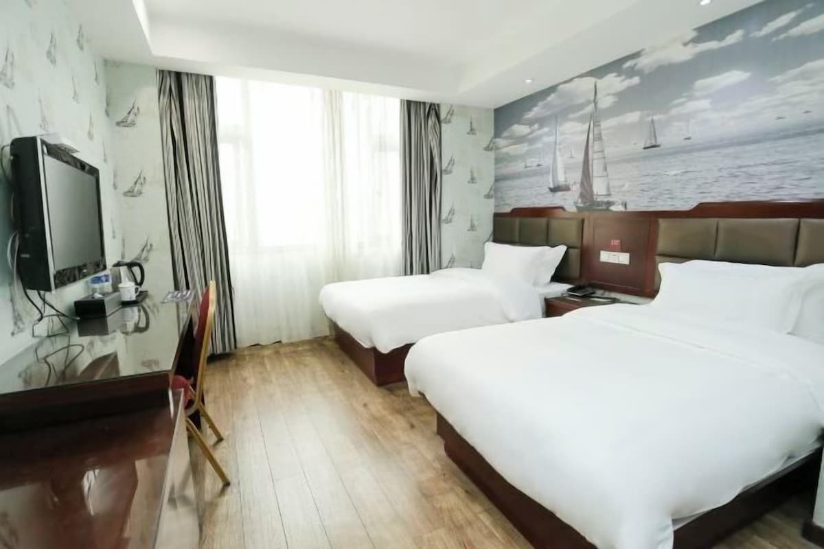 A hotel room with two beds, a desk with a television, and a mural of sailboats on the wall.