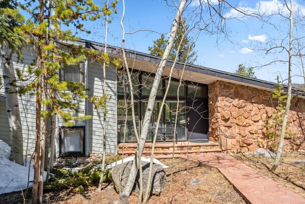 A modern house with a stone exterior, a wooden deck, and a stone pathway leading to the entrance.