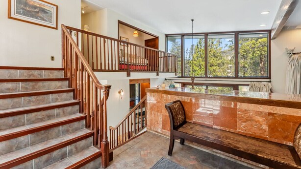 A spacious interior with a grand staircase, a marble reception desk, and large windows offering a view of the outdoors. - Spacious 4,000 Sq Ft Riverfront Home | Game Room • Deck • 1.5 Miles to Keystone (Keystone)