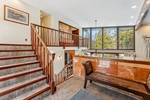 A spacious interior with a grand staircase, a marble reception desk, and large windows offering a view of the outdoors.