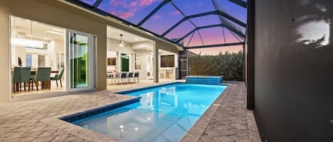 A swimming pool with a glass ceiling, a patio area with outdoor furniture, and a view of the sky.