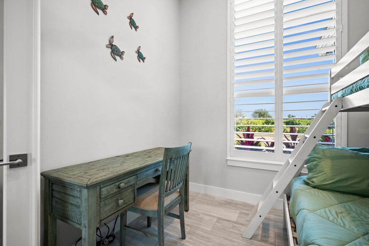 Una habitación con literas, un escritorio con silla y una ventana con persianas.