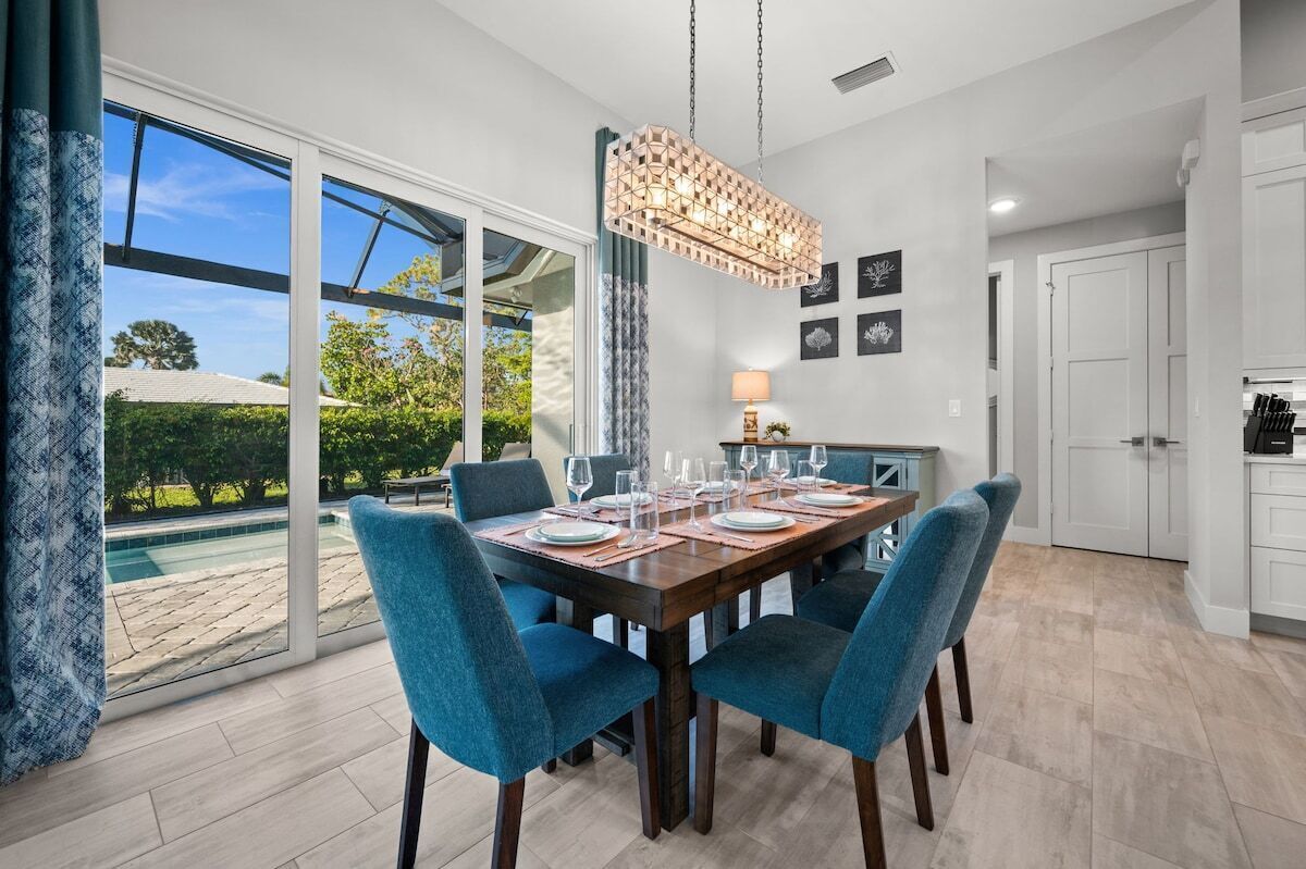 A dining area with a table set for four, a hanging light fixture, and a view of a swimming pool through large windows.
