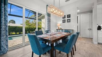A dining area with a table set for four, a hanging light fixture, and a view of a swimming pool through large windows.