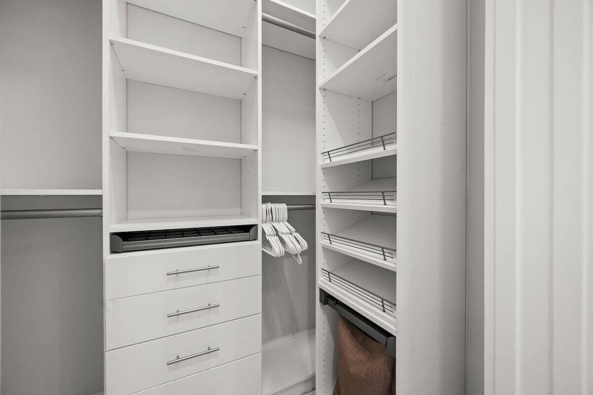 A white closet with open shelves and drawers, a hanging rack, and a towel rack.