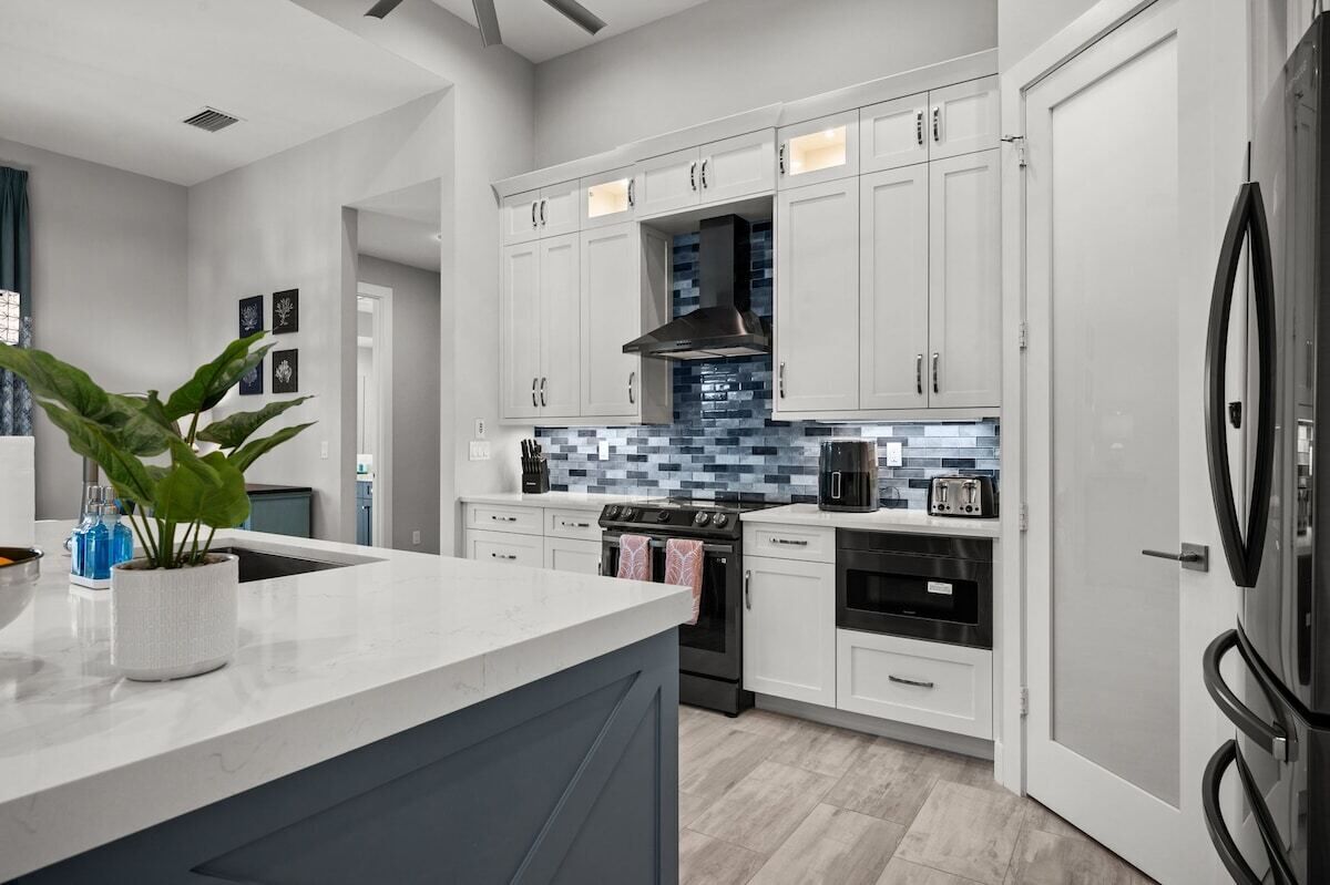 A modern kitchen with white cabinets, a stainless steel range hood, and a large refrigerator.