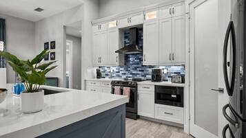 A modern kitchen with white cabinets, a stainless steel range hood, and a large refrigerator.