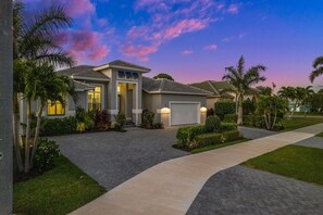 A residential house with a driveway, a garage, and a well-maintained lawn. - Modern Luxury • 7 Min to Beach • Heated Pool & Spa (Marco Island)