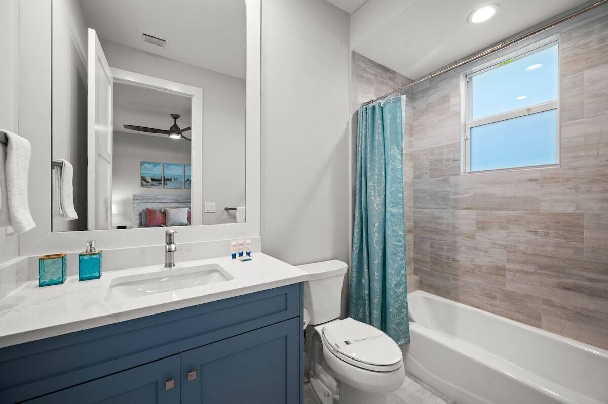 Un baño con un lavamanos blanco, armarios azules, inodoro y bañera.