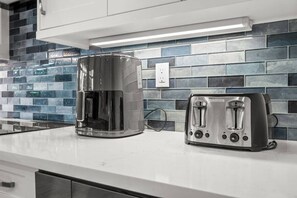 A kitchen with a coffee maker and a toaster on the counter, a tiled backsplash, and a white countertop. - Modern Luxury • 7 Min to Beach • Heated Pool & Spa (Marco Island)