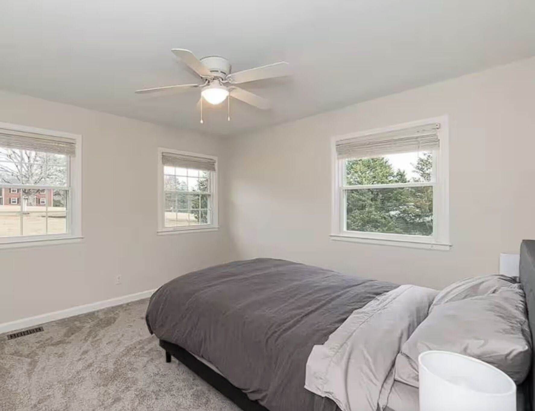 Un dormitorio con una cama, ventilador de techo y tres ventanas.