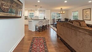 A spacious living room with a large sofa and a dining area with chairs and a table. There is a kitchen in the background with a bar counter. - Family Retreat - 3-bedroom unit with NEW Pool, WiFi and AC in North Durham (Durham)