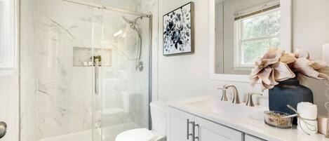 A bathroom with a glass-enclosed shower, a white toilet, and a vanity with a mirror and sink.