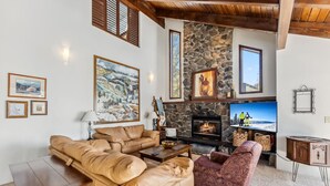 A cozy living room with a stone fireplace, leather sofas, and a television. - Spacious Forest-Backed Lodge • 5BR • Game Room • Minutes to Slopes (Keystone)