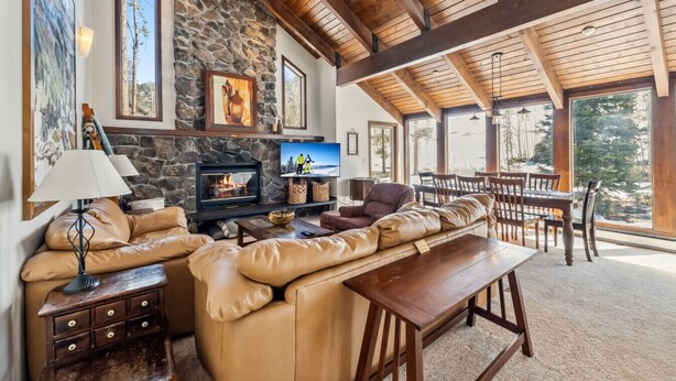 A cozy living room with a stone fireplace, leather sofa, and wooden dining table. - Spacious Forest-Backed Lodge • 5BR • Game Room • Minutes to Slopes (Keystone)