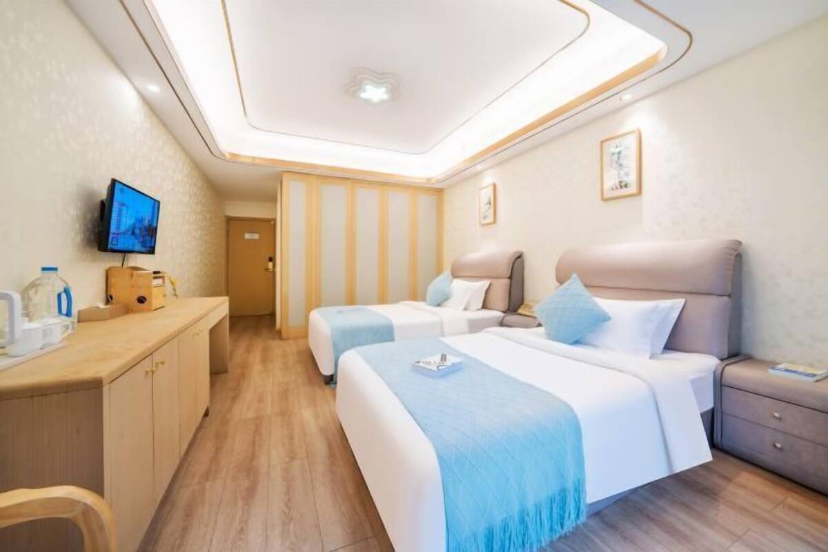 A hotel room with two beds, a desk, a television, and a ceiling light fixture.