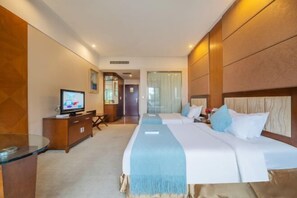 A hotel room with a large bed, a TV, a desk, and a view of the hallway.
