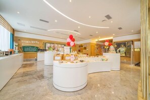 Een hotel lobby met een receptiebalie, een gebogen toonbank met presentatiestukken en een muur met informatieposters.