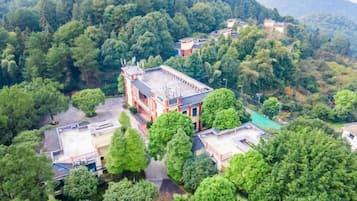 A building surrounded by dense greenery, with multiple structures and a clear sky.