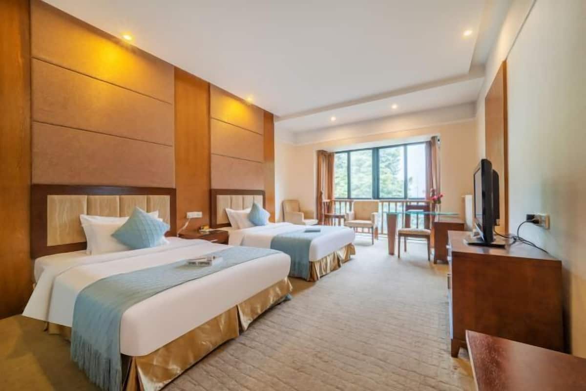 A hotel room with two beds, a TV, a desk, and a balcony with a view.