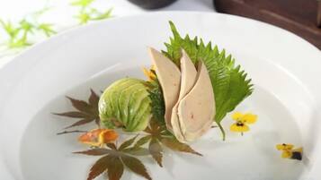 A white plate with a decorative arrangement including a green fruit, leaves, and small flowers.