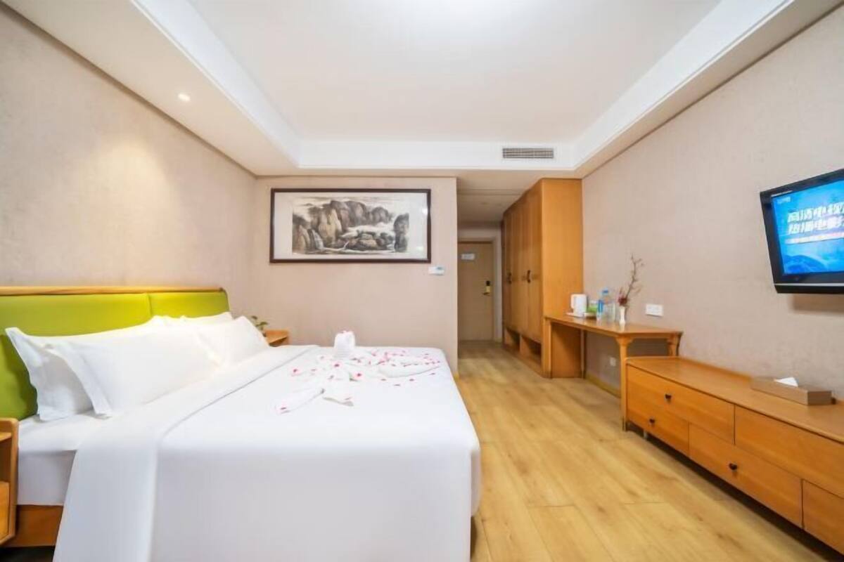 A hotel room with a bed, a television, a wooden dresser, and a painting on the wall.