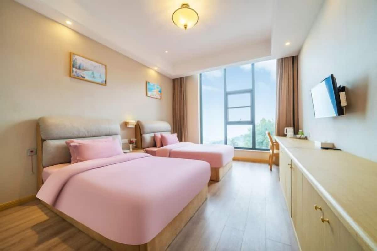 A modern hotel room with two beds, a large window, a flat-screen TV, and a wooden cabinet.