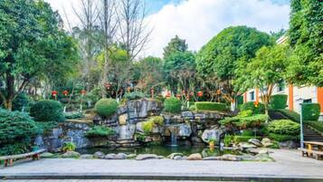 Un jardín ajardinado con un estanque, bancos y diversas especies de árboles y arbustos.