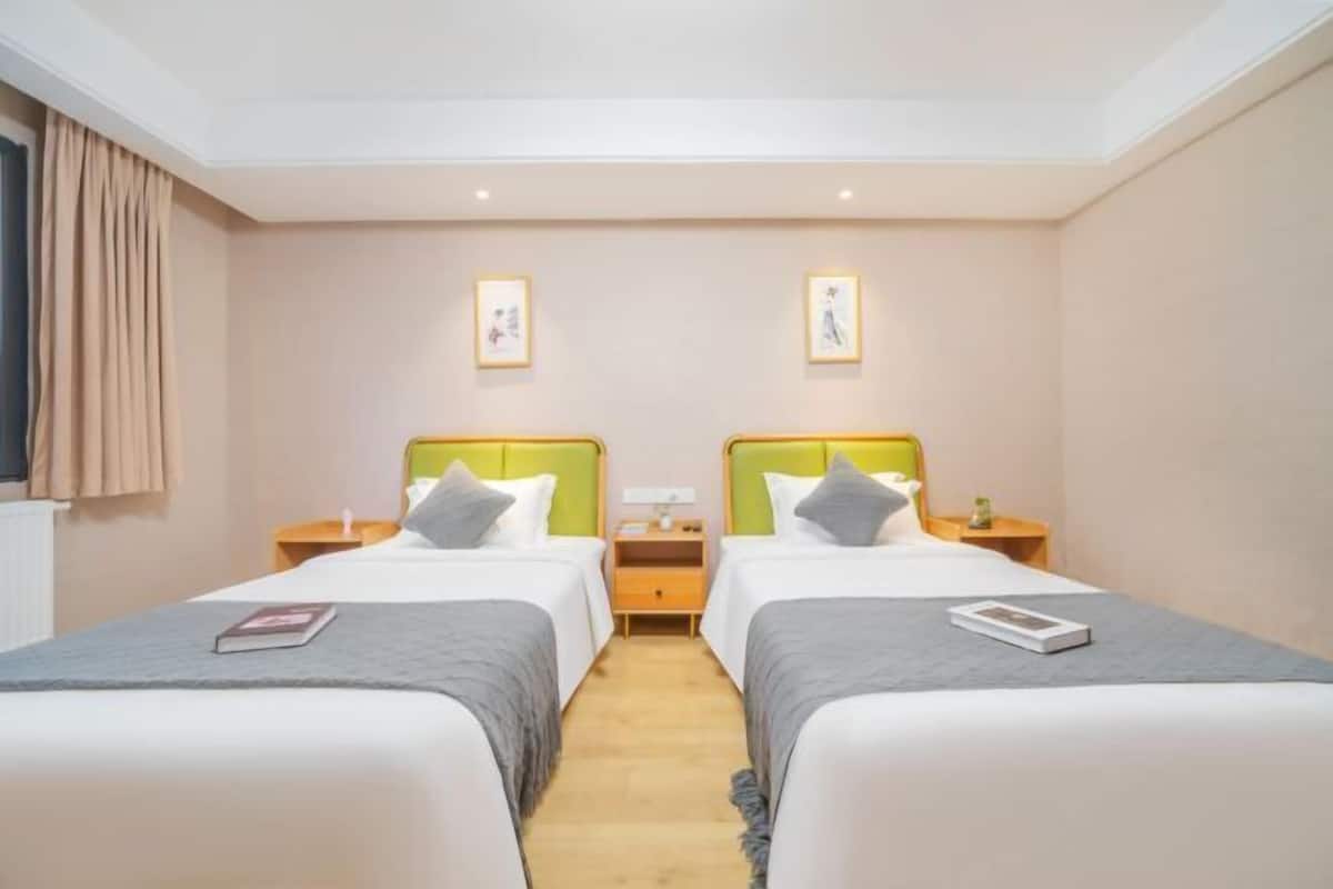 A hotel room with two single beds, a nightstand with a lamp, and a framed picture on the wall.