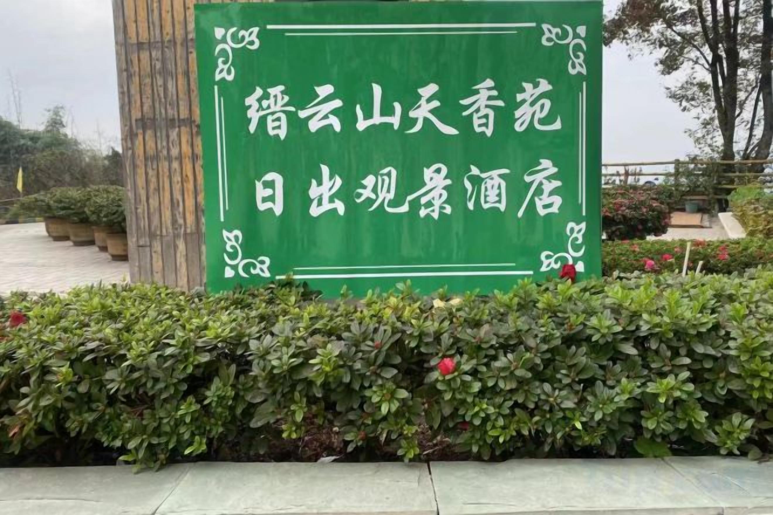 Un letrero verde con texto blanco, rodeado de un seto.