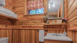 Une salle de bain de style rustique, avec des murs en bois, comprenant des toilettes, un lavabo et un miroir.