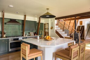 Une cuisine moderne dotée d’un îlot central, de chaises en bois et d’un escalier menant à un niveau supérieur.