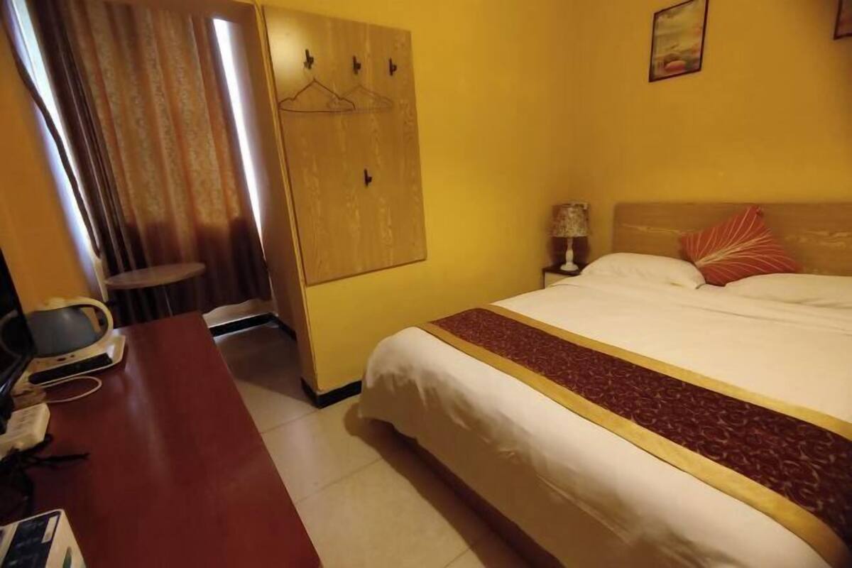 Ein Hotelzimmer mit einem Bett, einem Schreibtisch mit Telefon, einem Kleiderständer und einem an der Wand hängenden Kunstwerk.