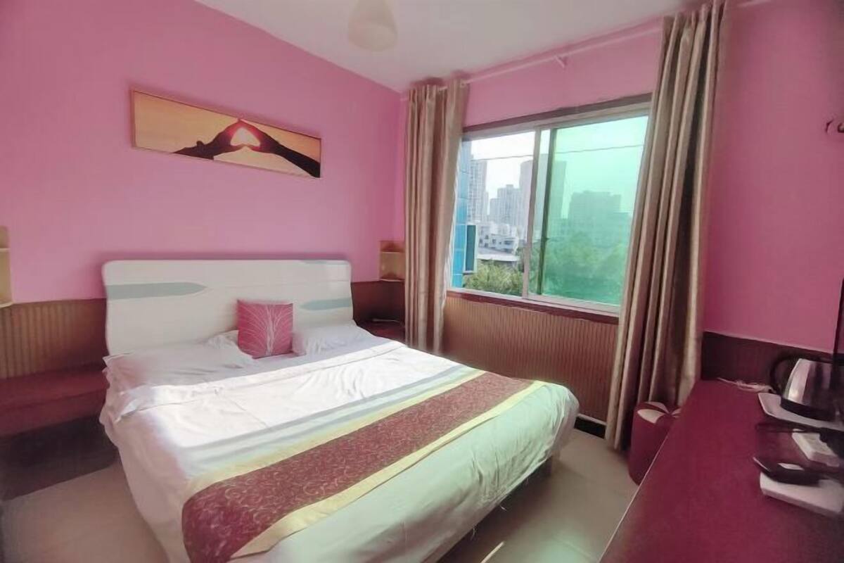 Ein Hotelzimmer mit Bett, Schreibtisch, einem Fenster mit Vorhängen und einem Gemälde an der Wand.