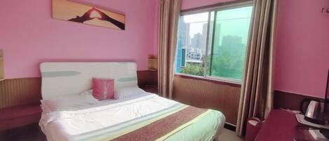 A hotel room with a bed, a desk, a window with curtains, and a painting on the wall.