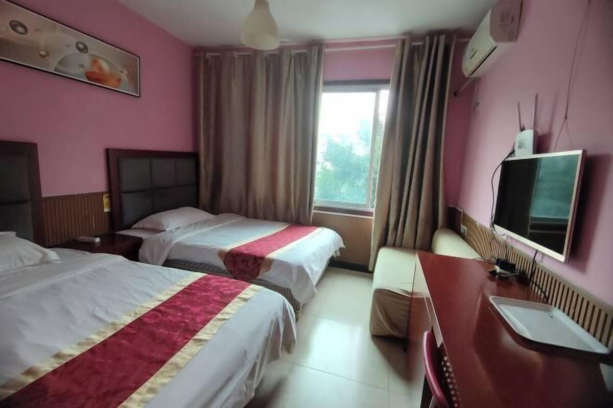 Ein Hotelzimmer mit zwei Betten, einem Schreibtisch, einem Stuhl, einem Fernseher und einem Fenster mit Vorhängen.