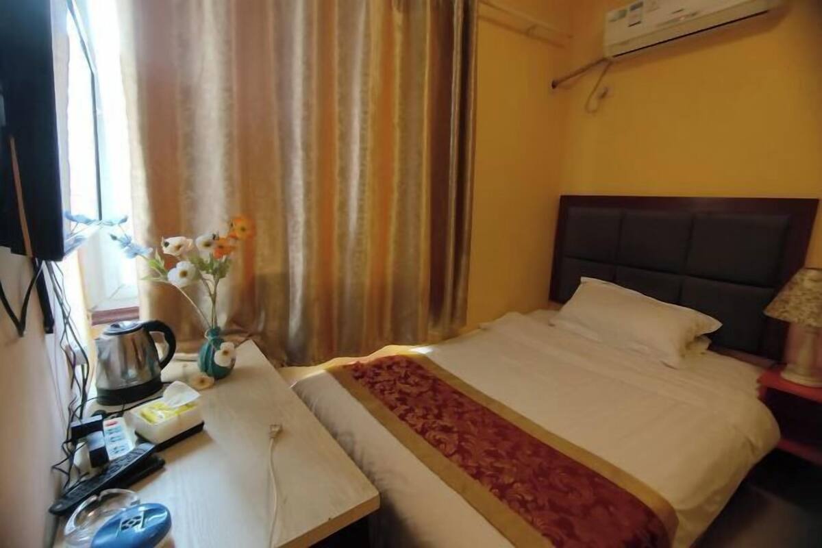Ein Hotelzimmer mit Bett, Schreibtisch mit Wasserkocher, Blumen in einer Vase und einer Klimaanlage.