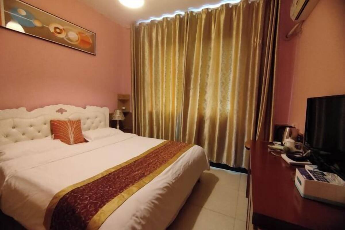 Ein Hotelzimmer mit einem großen Bett, einem Fernseher, einem Schreibtisch mit Telefon und einem Vorhang.