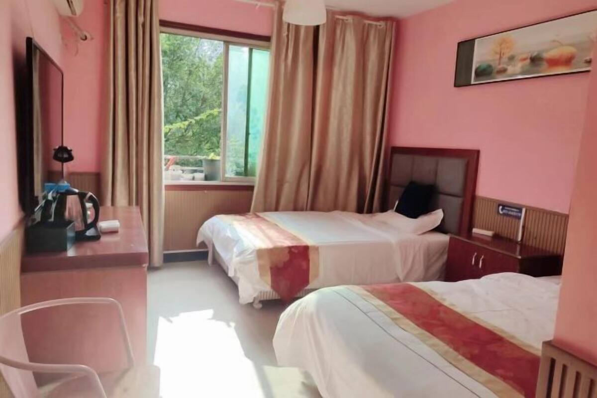 Ein Hotelzimmer mit zwei Betten, einem Schreibtisch, einem Stuhl, einem Fenster mit Vorhängen und einem Bild an der Wand.