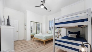 A bedroom with two bunk beds, a ceiling fan, a TV on a cabinet, and a window with blinds. - Oh Whale Pawleys Island SC (Pawleys Island)