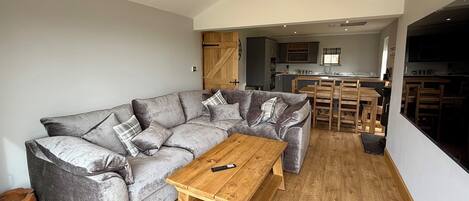 Un salon moderne avec un canapé d’angle gris, une table basse en bois et un coin repas comprenant des chaises et une table en bois.