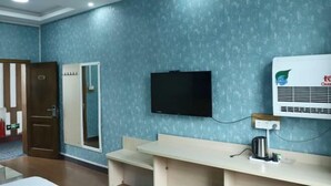 Een hotelkamer met een blauwe structuurwand, een flatscreen televisie boven een houten bureau en een luchtverwarmer aan de muur.