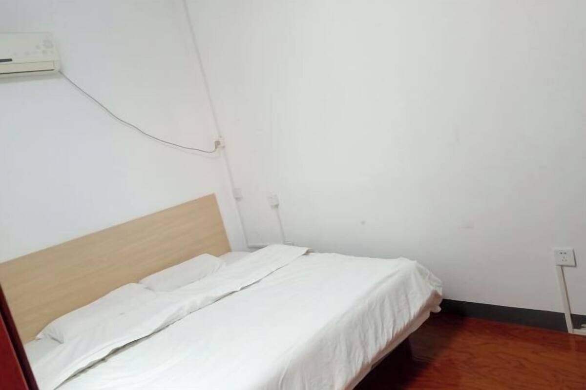 Un lit simple avec une tête de lit en bois, dans une pièce aux murs blancs et au plancher en bois.