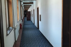 Un pasillo con alfombra estampada, puertas a la derecha y extintor a la izquierda.