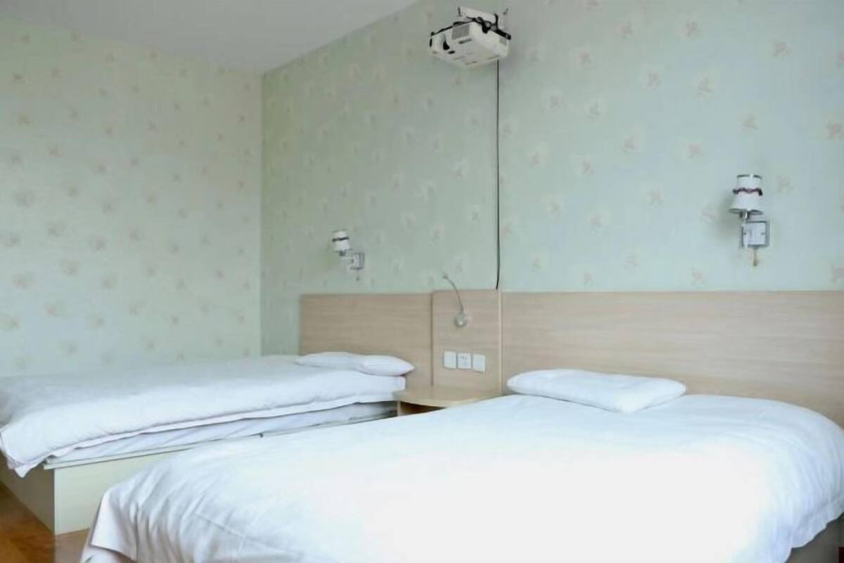 Une chambre d’hôtel avec deux lits, un projecteur fixé au plafond et un luminaire fixé au mur.