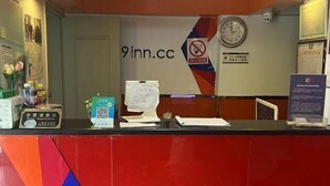 A hotel reception desk with a clock, a sign for 9inn.cc, and a registration area with a computer and documents.