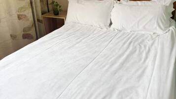 Uma cama com roupa de cama branca, cabeceira de madeira e mesa de cabeceira com uma planta.